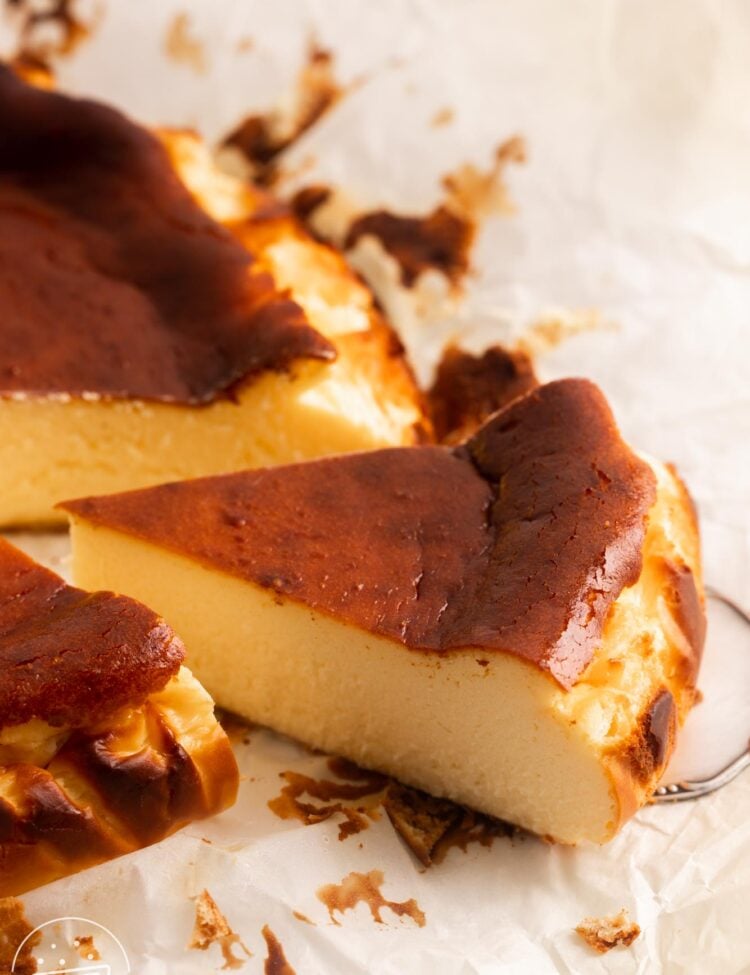 a slice of basque cheesecake with a caramelized brown top, pulled away from the whole cake with a cake server.