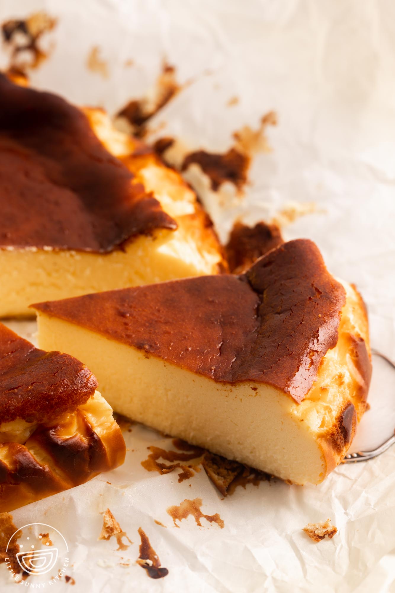 a slice of basque cheesecake with a caramelized brown top, pulled away from the whole cake with a cake server.