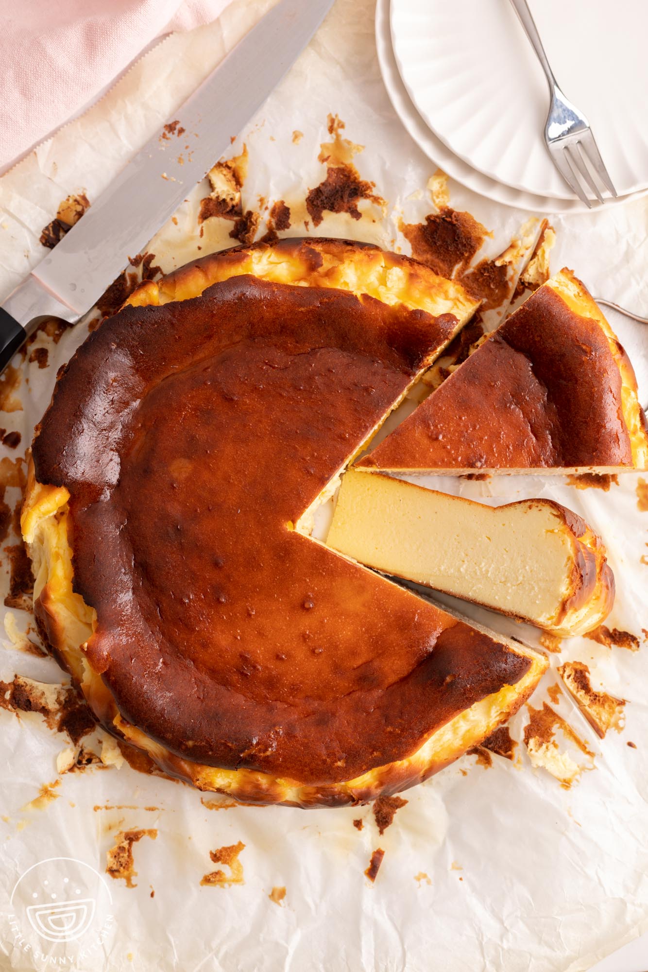 a basque cheesecake with brown top on a piece of parchment, slices have been cut from the right side.