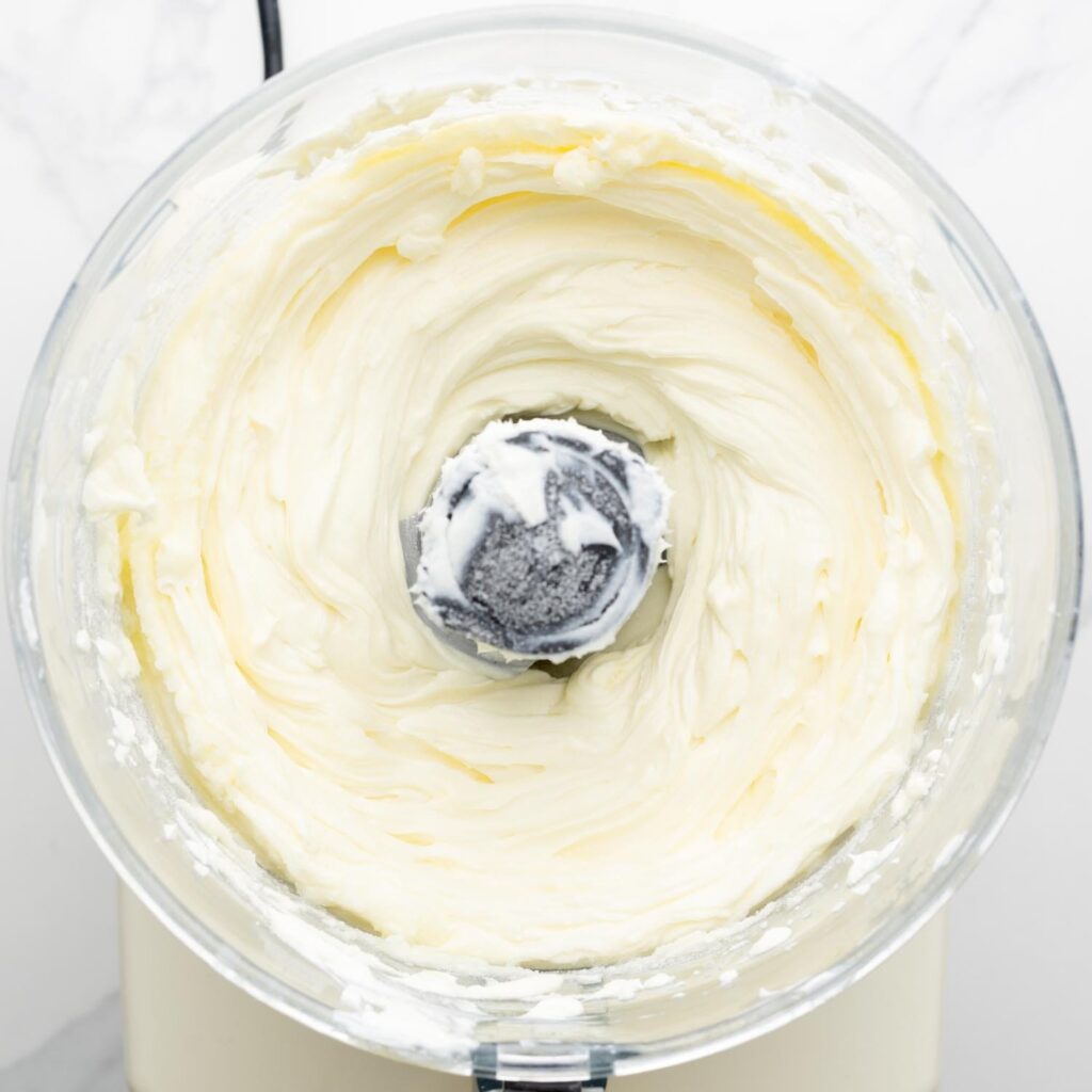 cream cheese and sugar mixed in the bowl of a food processor.