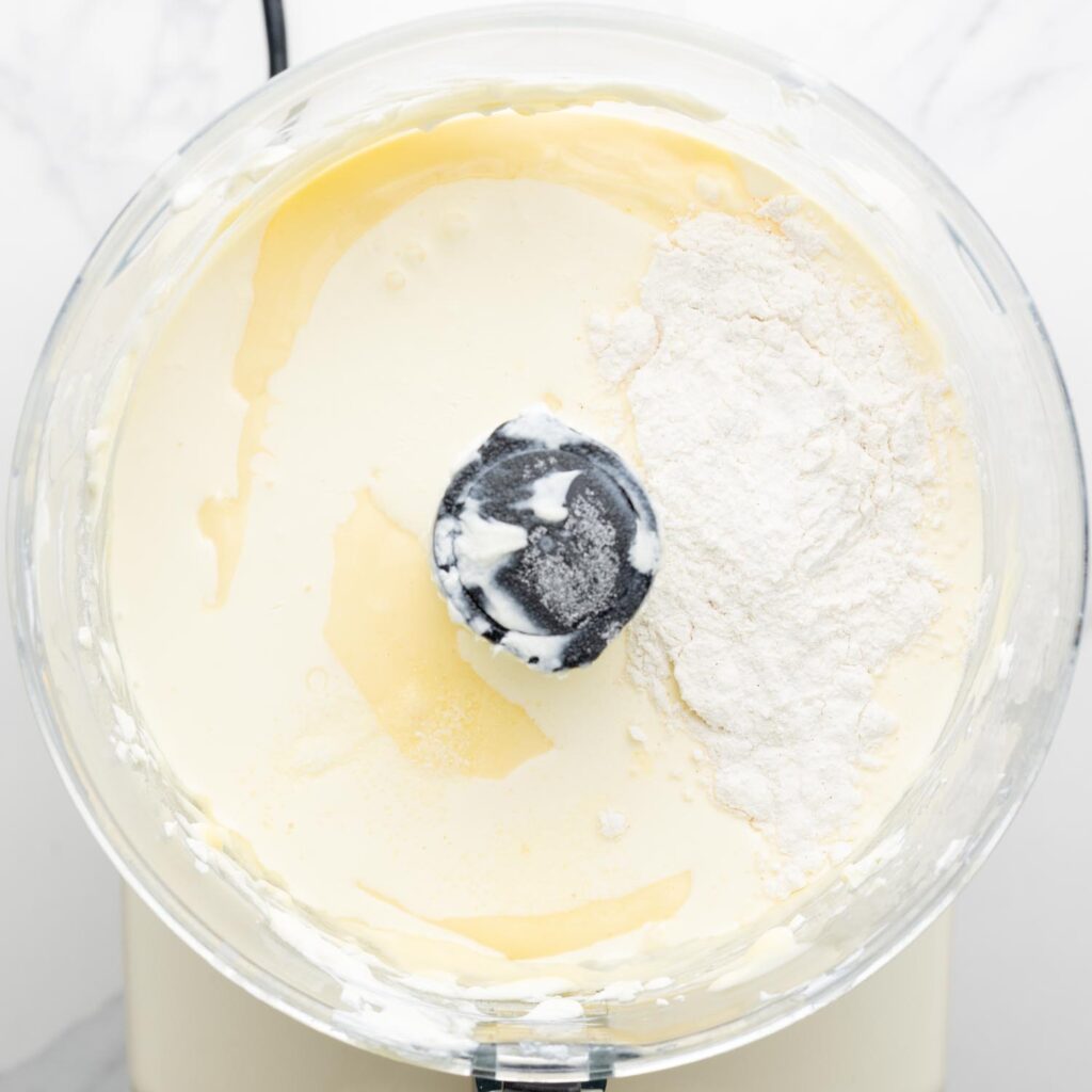 cream and flour added to cheesecake ingredients in a food processor.