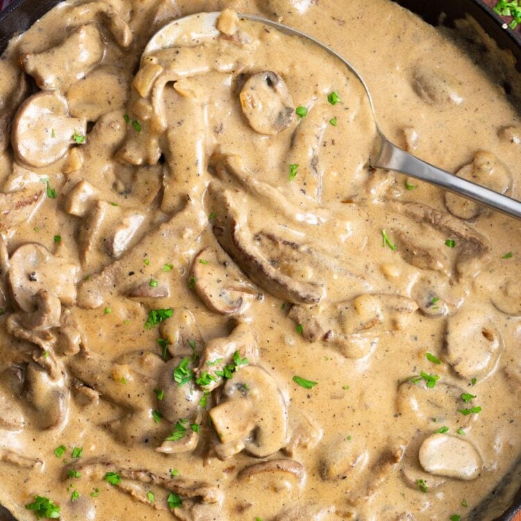 a spoon serving beef stroganoff from a skillet.