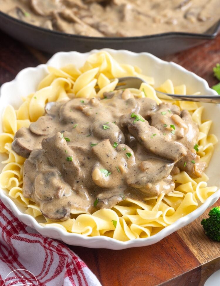 a fluted white bowl filled with egg noodles and beef stroganoff.