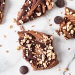 uneven pieces of frozen chocolate bark on a marble counter. The yogurt bark is topped with melted chocolate drizzle and chopped toffee bits.