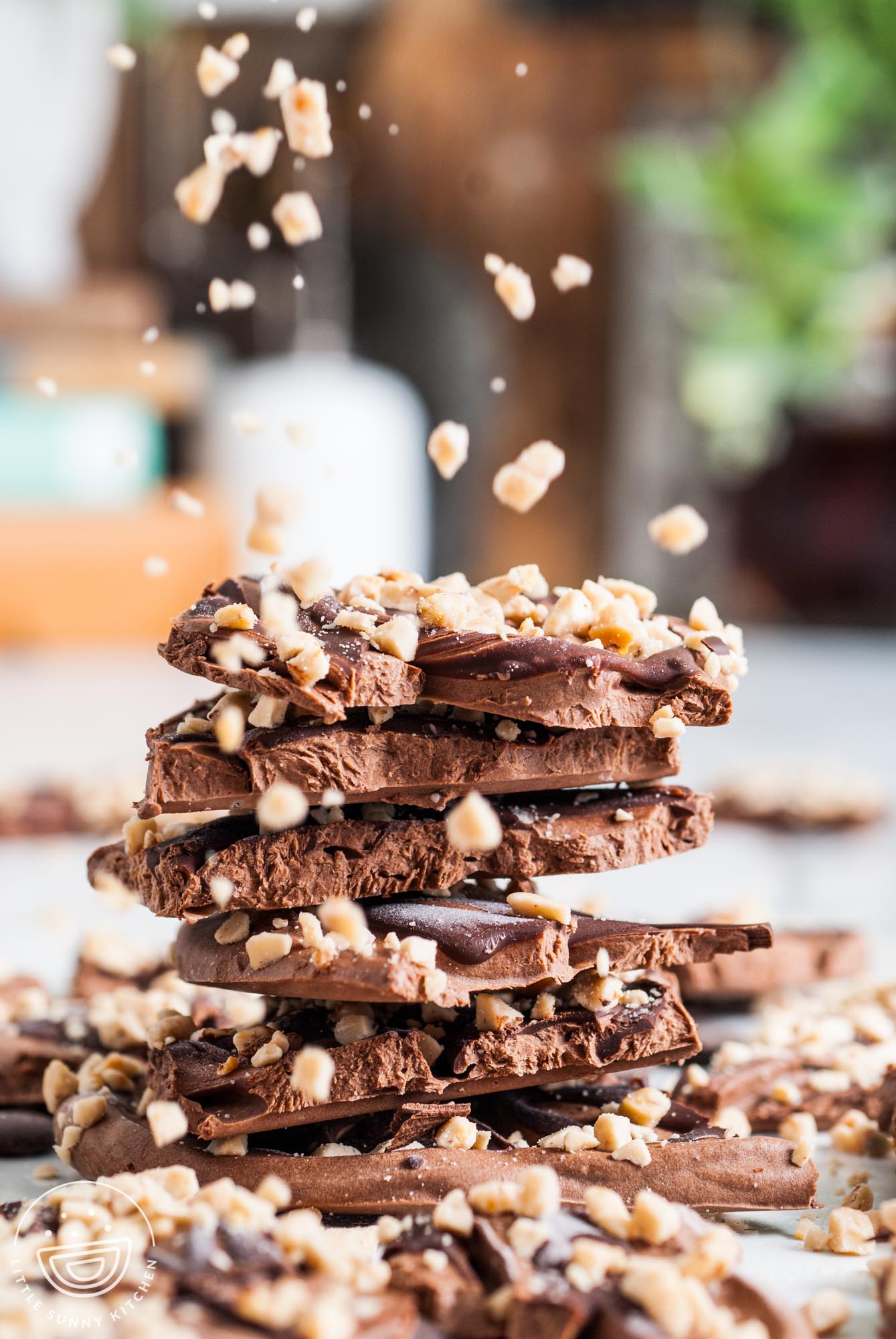 a stack of chocolate frozen yogurt bark pieces. Toffee bits are being sprinkled over them.