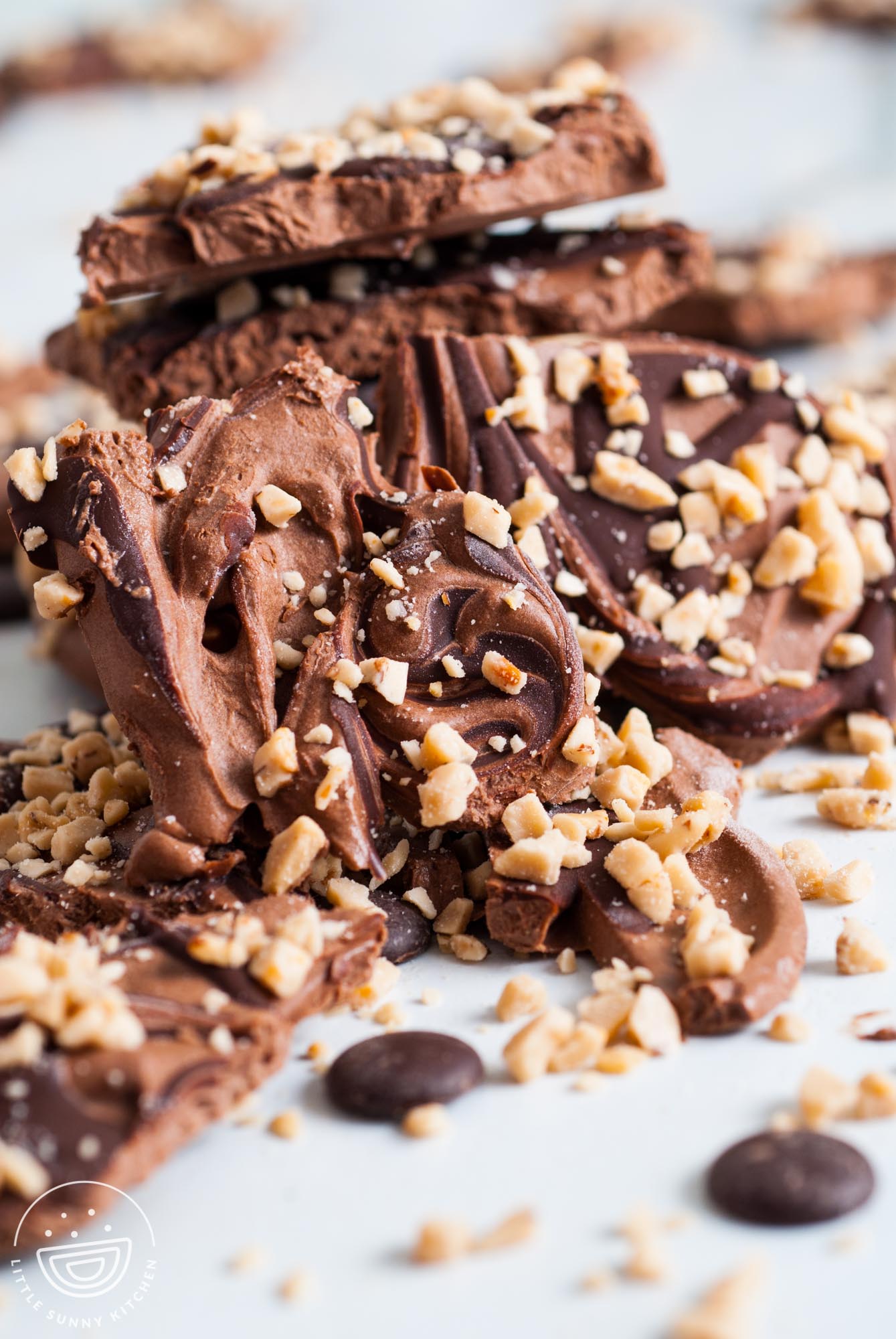 Pieces of frozen chocolate yogurt bark on a white surface, topped with swirled chocolate and chopped toffee bits.