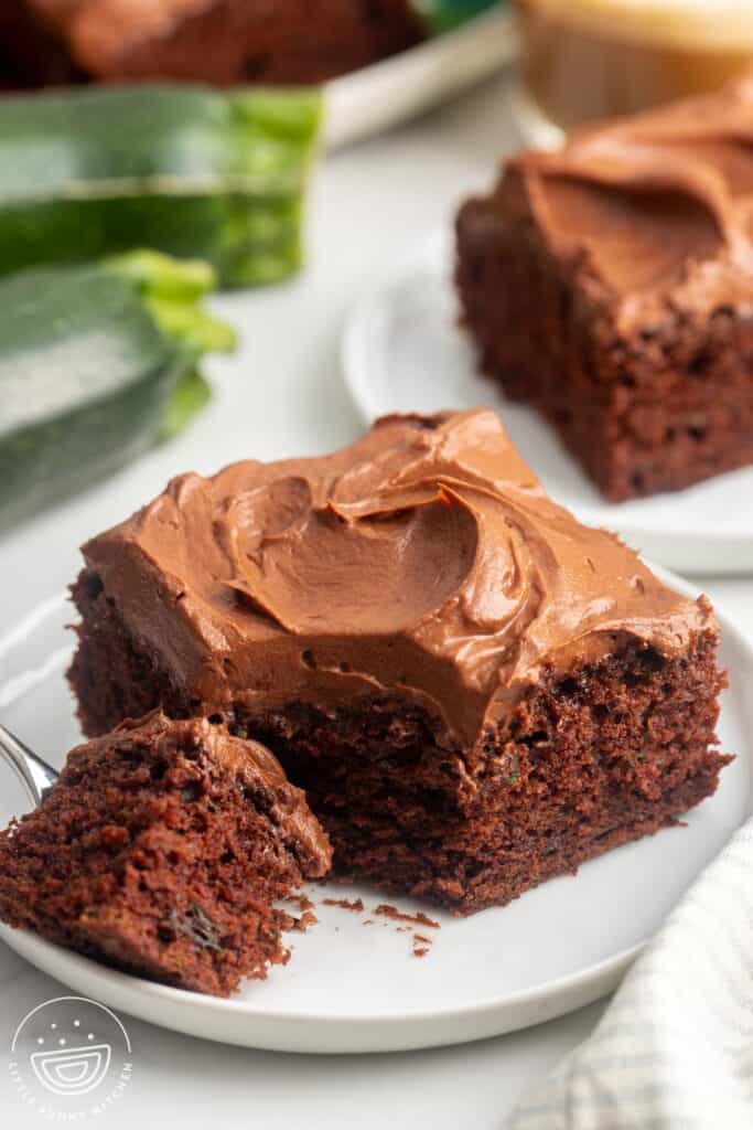 a square piece of chocolate zucchini cake with frosting. A fork has removed a bite from the corner.