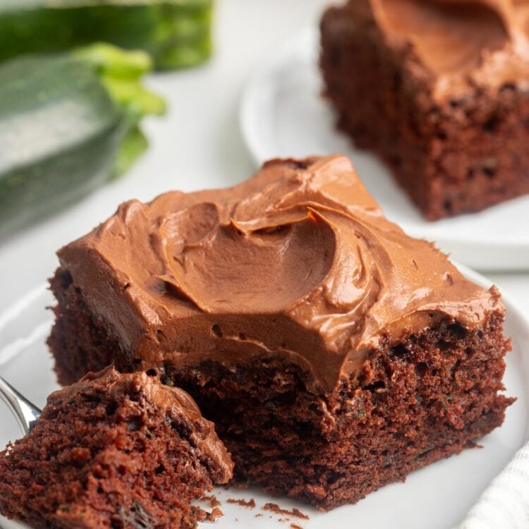 a square piece of chocolate zucchini cake with frosting. A fork has removed a bite from the corner.