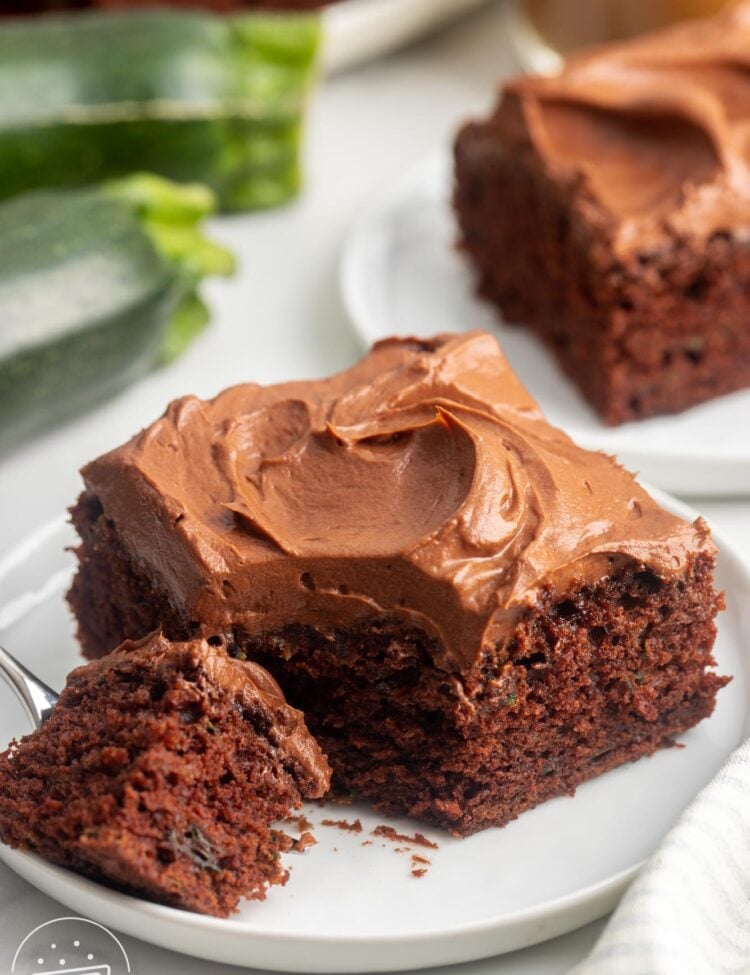 a square piece of chocolate zucchini cake with frosting. A fork has removed a bite from the corner.