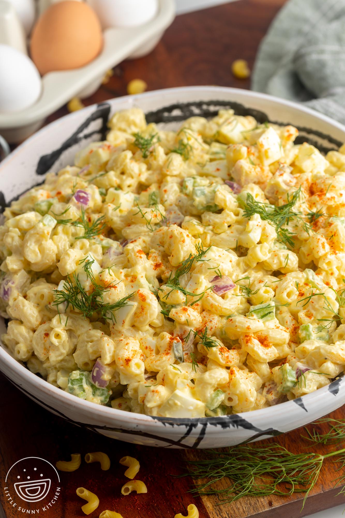 a large bowl of deviled egg pasta salad next to a carton of eggs.