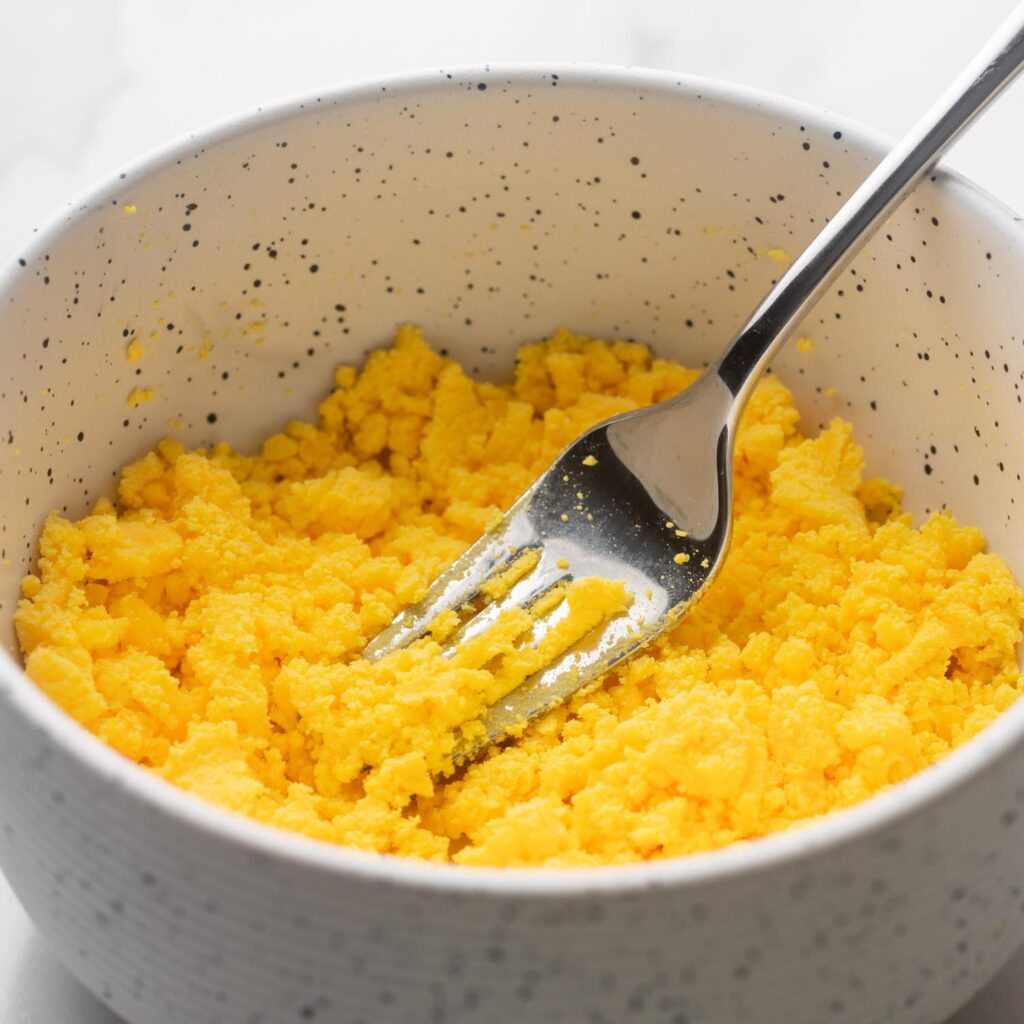 a fork mashing hard cooked egg yolks in a small bowl.