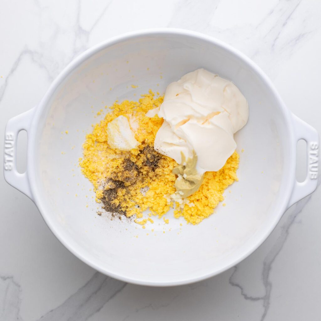 mashed egg yolks, mayo, mustard, seasonings in a large white mixing bowl.