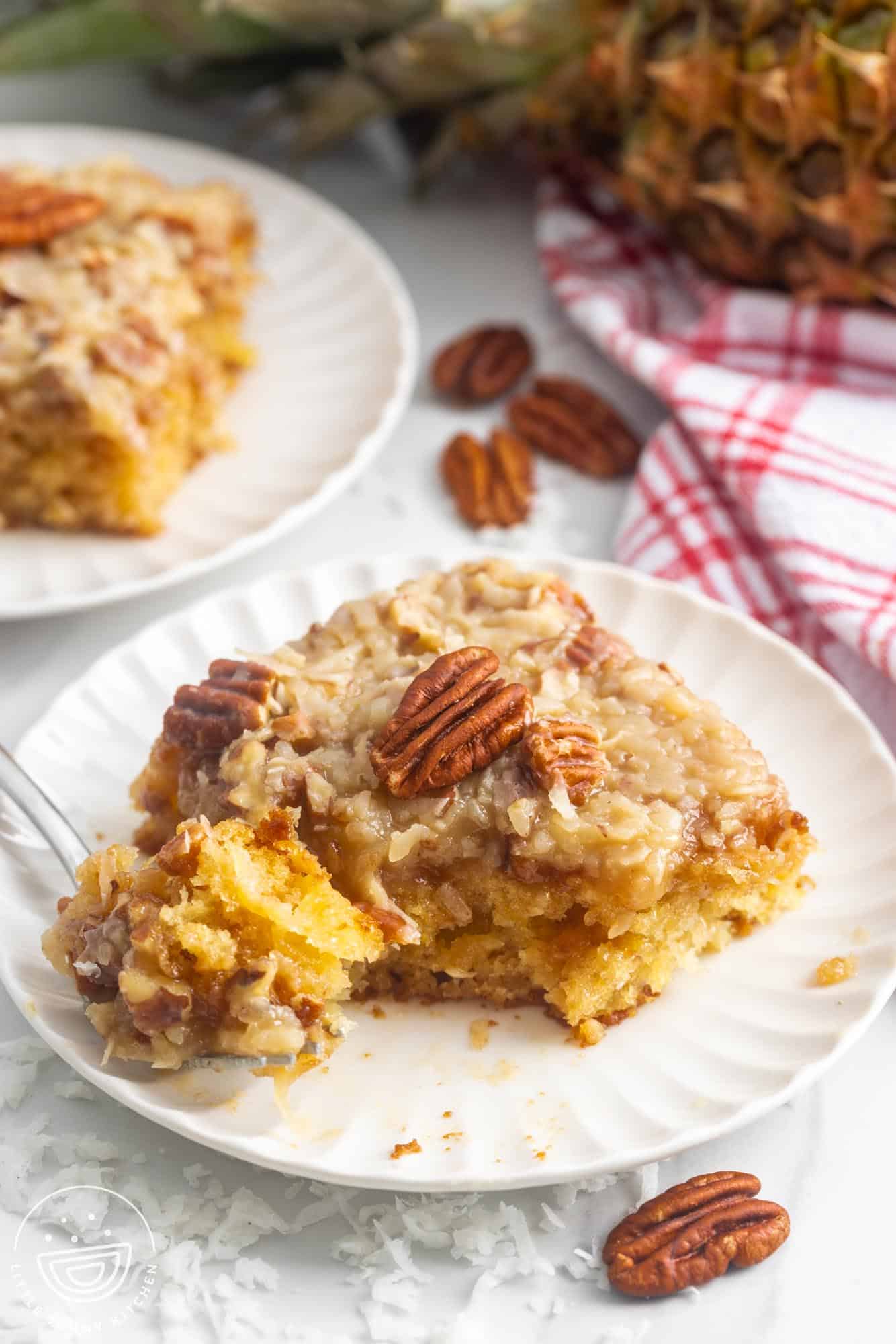 A square slice of do nothing cake on a plate, topped with coconut frosting and toasted pecans.