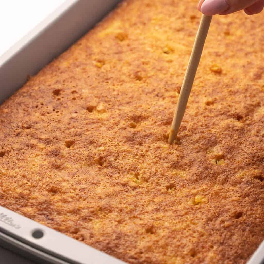 A chopstick poking holes into a baked cake.