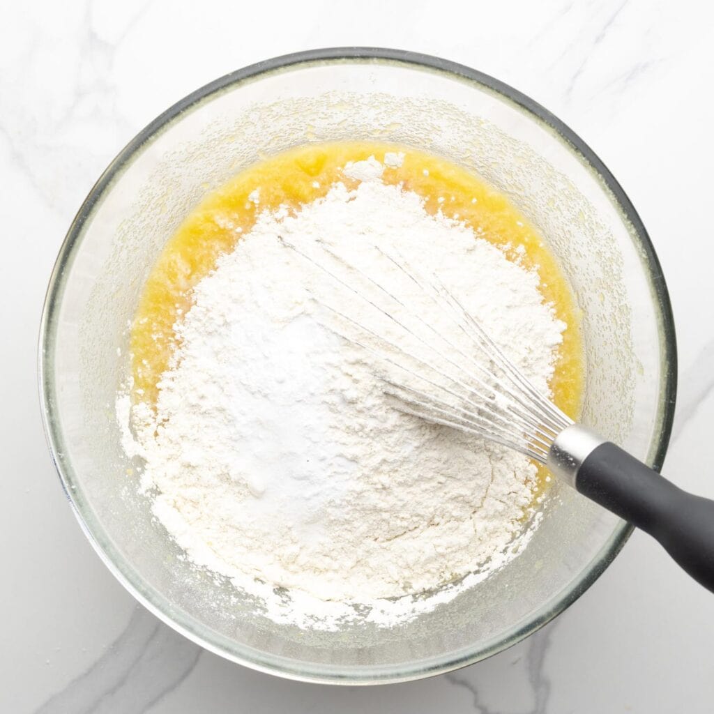 Dry Ingredients added to wet ingredients with a whisk in a glass mixing bowl.