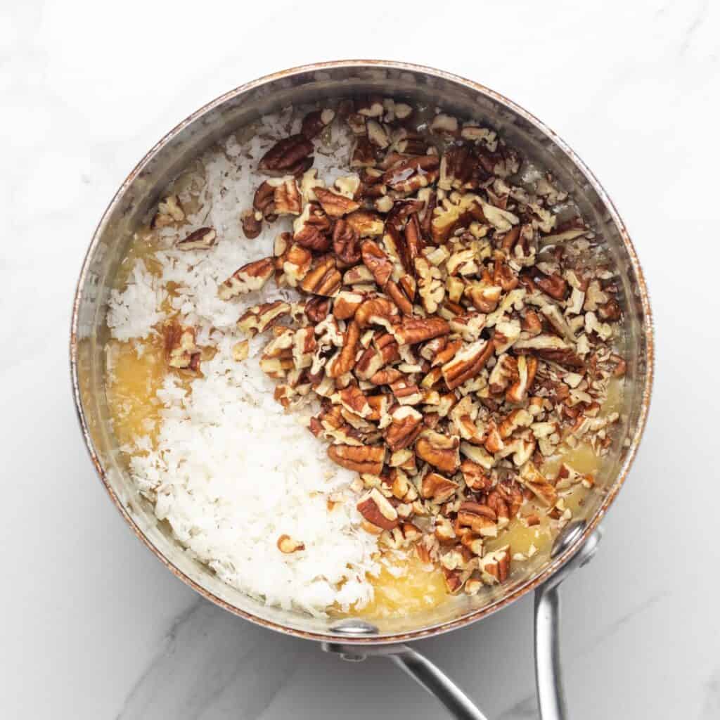 Pecans and shredded coconut added to melted butter and sugar in a saucepan.