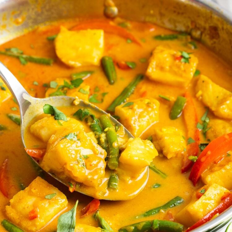 Thai fish curry with green beans and red peppers in a stainless steel skillet.