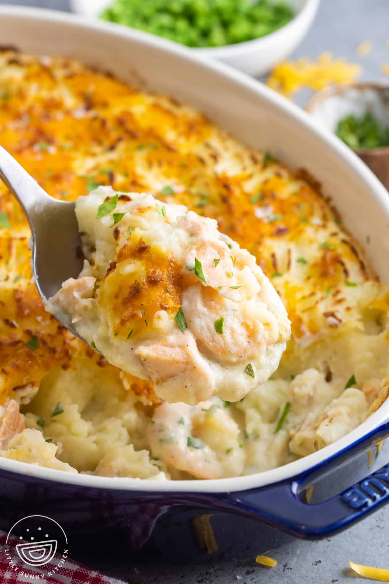 a dark blue casserole dish of british fish pie, served with a metal spoon.