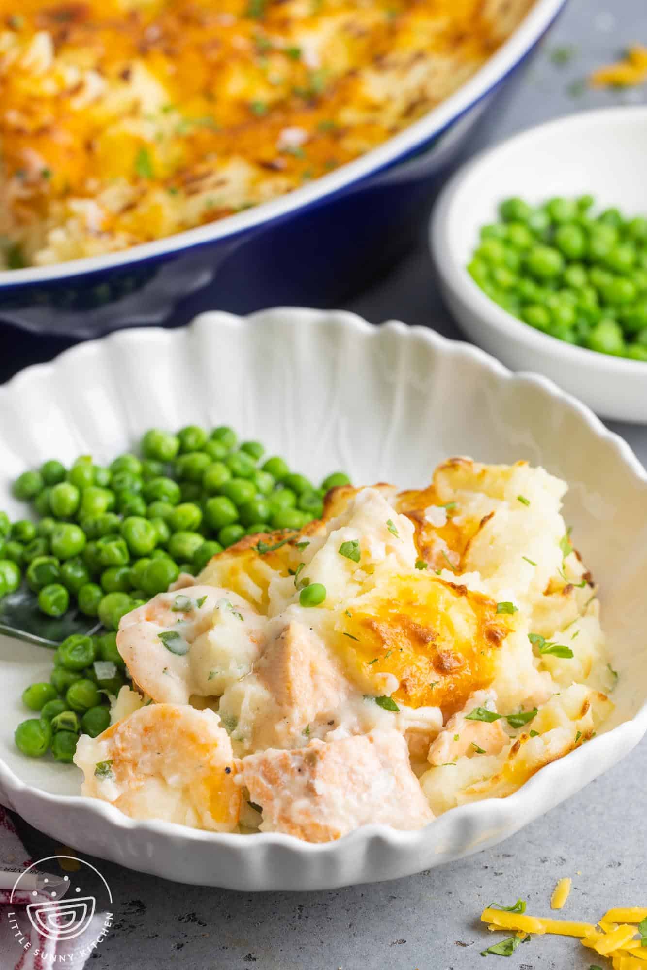 a shallow white bowl with a serving of fish pie and peas.