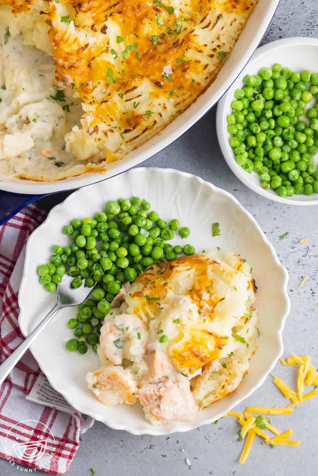 a plate of fish pie with steamed green peas.