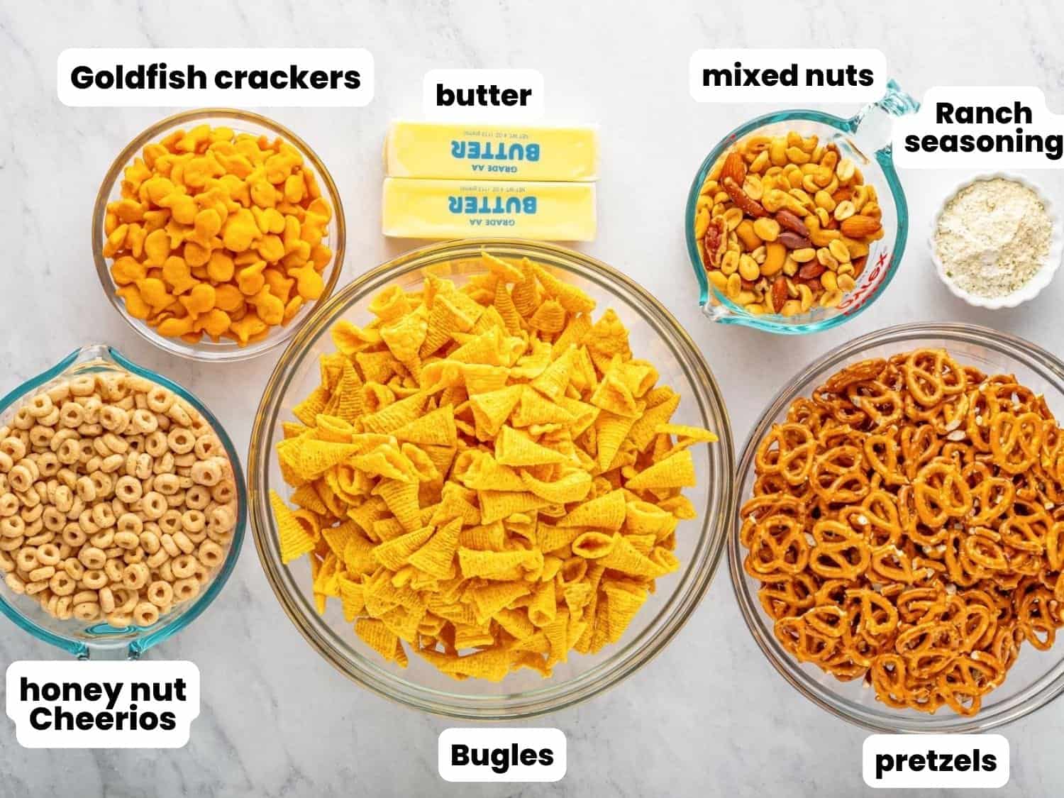 The ingredients needed to make Ranch snack mix with Bugles, including pretzels, nuts, butter, goldfish crackers, and honey nut cheerios.