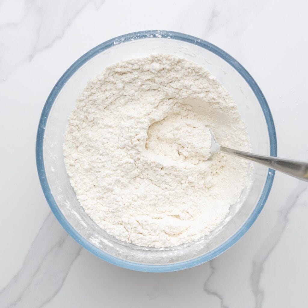 A glass bowl filled with flour, stirred with a fork.