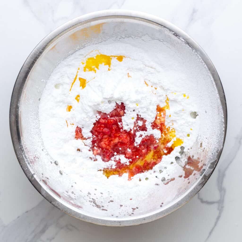 powdered sugar, melted butter, and lemon juice added to mashed strawberries in a metal mixing bowl.