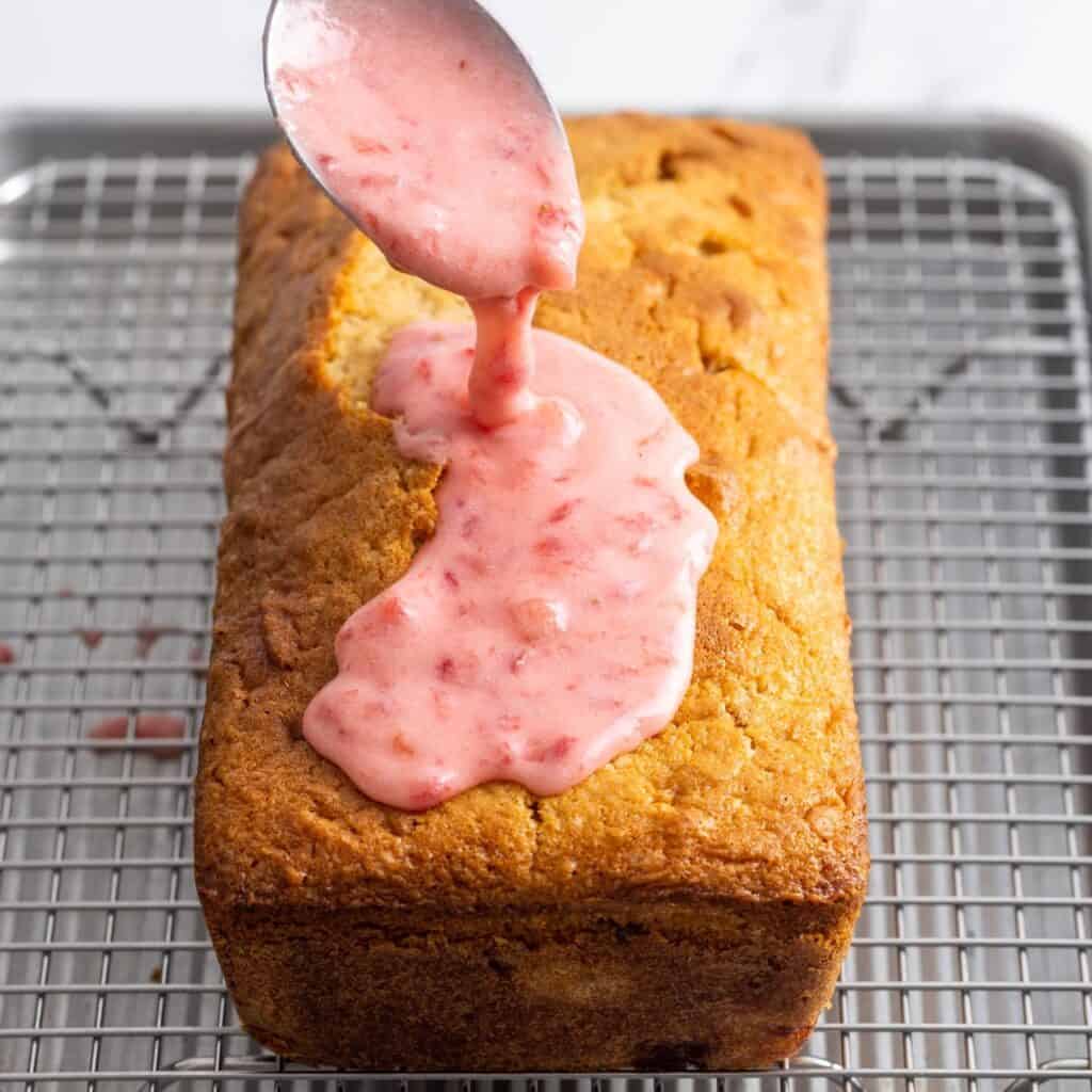 a spoon adding strawberry glaze to the top of a loaf of pound cake.