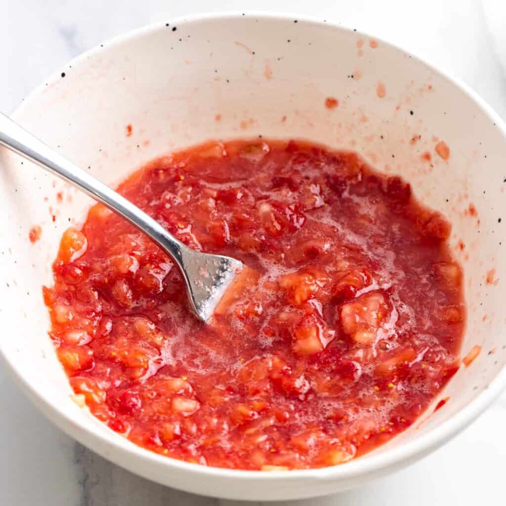 diced strawberries mashed with a fork in a small white bowl.