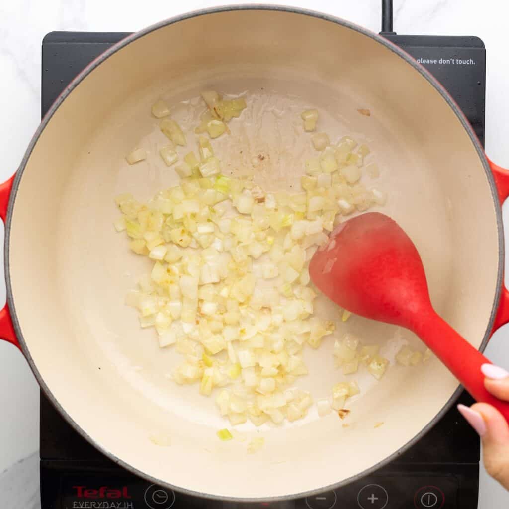 diced onion sauteed in a dutch oven stirred with a red spoon.