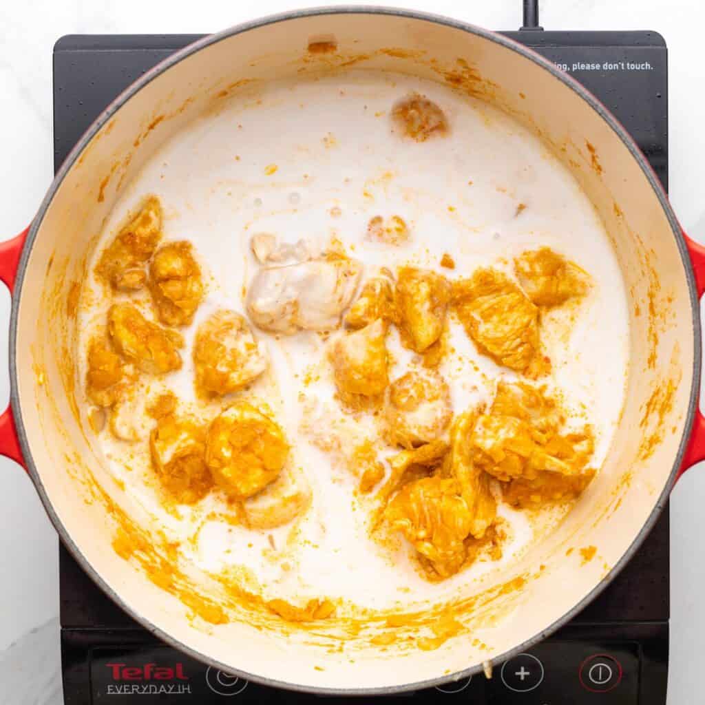 Coconut milk added to a dutch oven of curry seasoned cooked chicken.