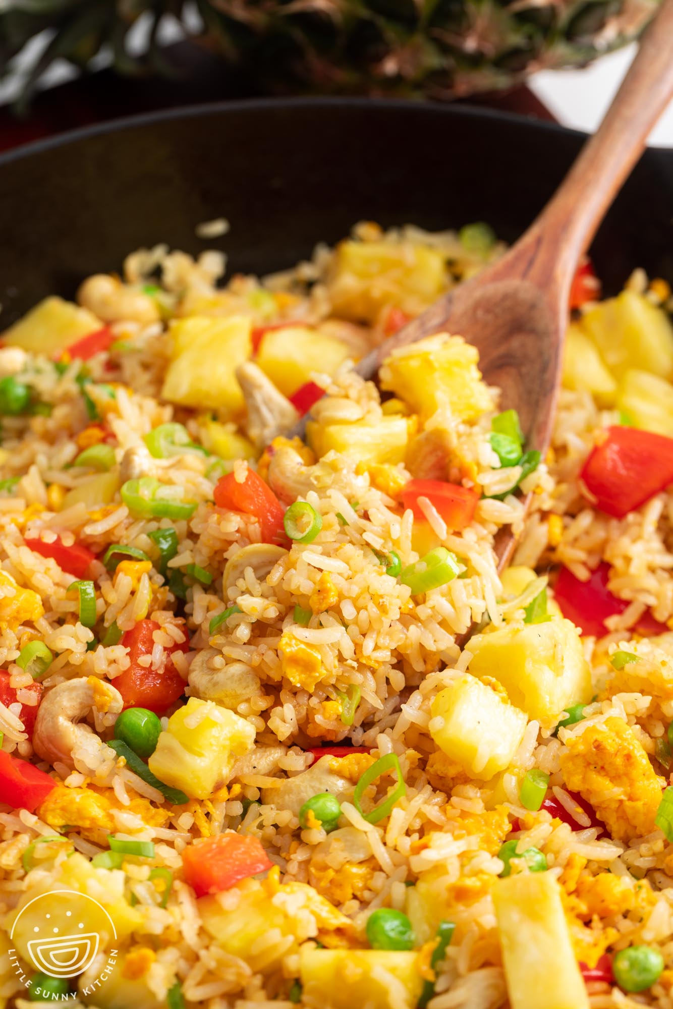 a wooden spoon stirring Thai fried rice with pineapple, peppers, and peas.