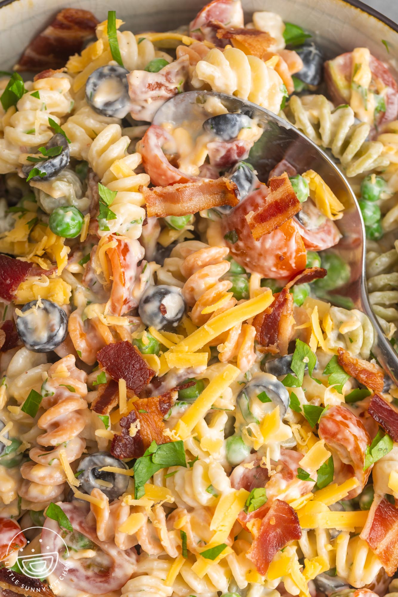 closeup of bacon ranch pasta salad, showing large pieces of real bacon, shredded cheese, and sliced black olives.