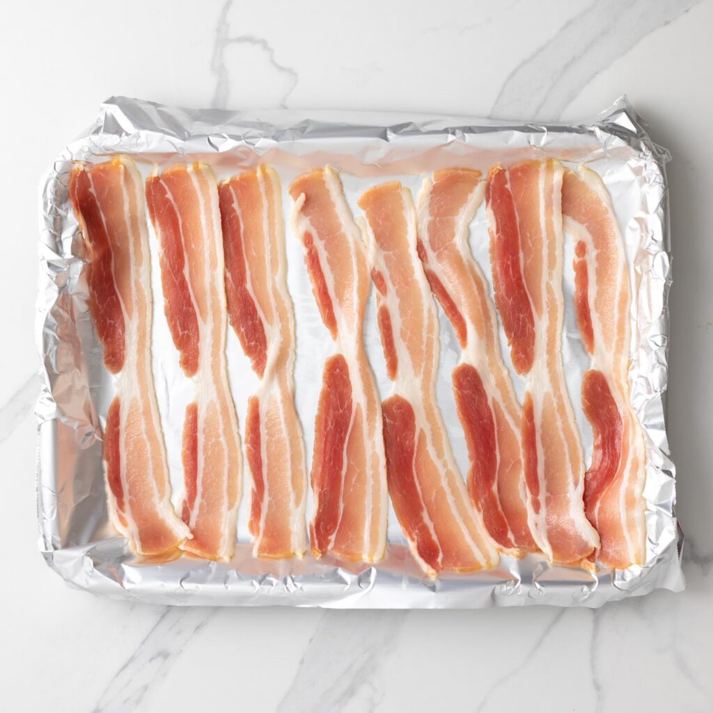 8 slices of raw bacon on a foil lined baking sheet.