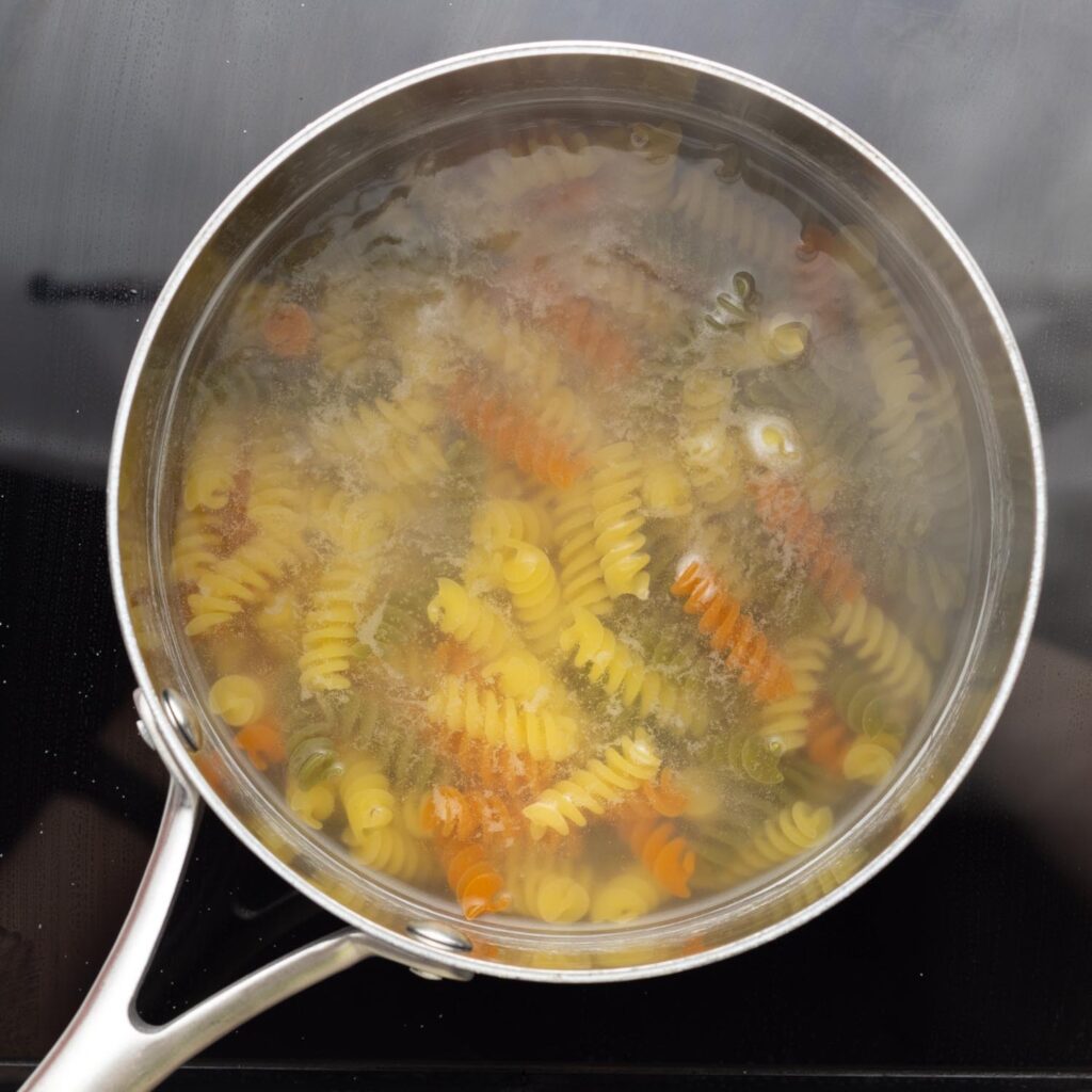 tricolor rotini pasta cooking in a saucepan.