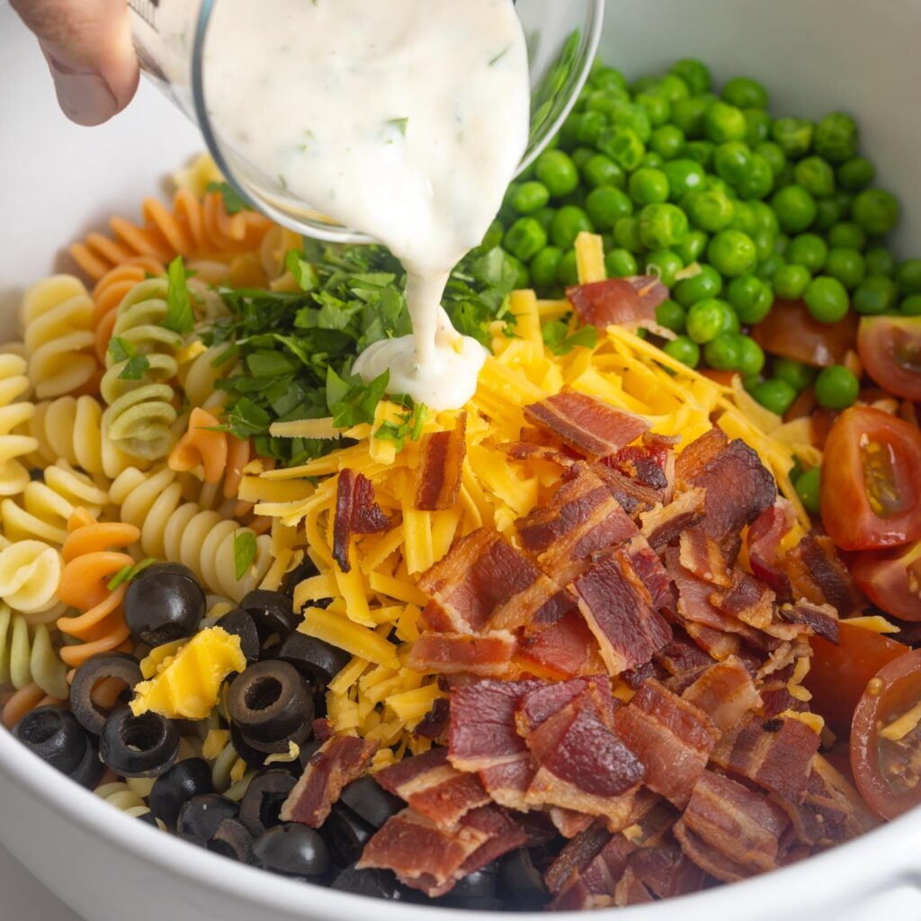 ranch dressing poured over pasta salad ingredients.