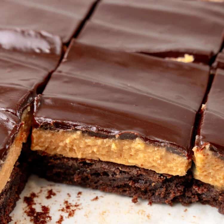 closeup of a cut pan of buckeye brownies. Two pieces have been removed to show the layers of brownie, peanut butter, and chocoalate.