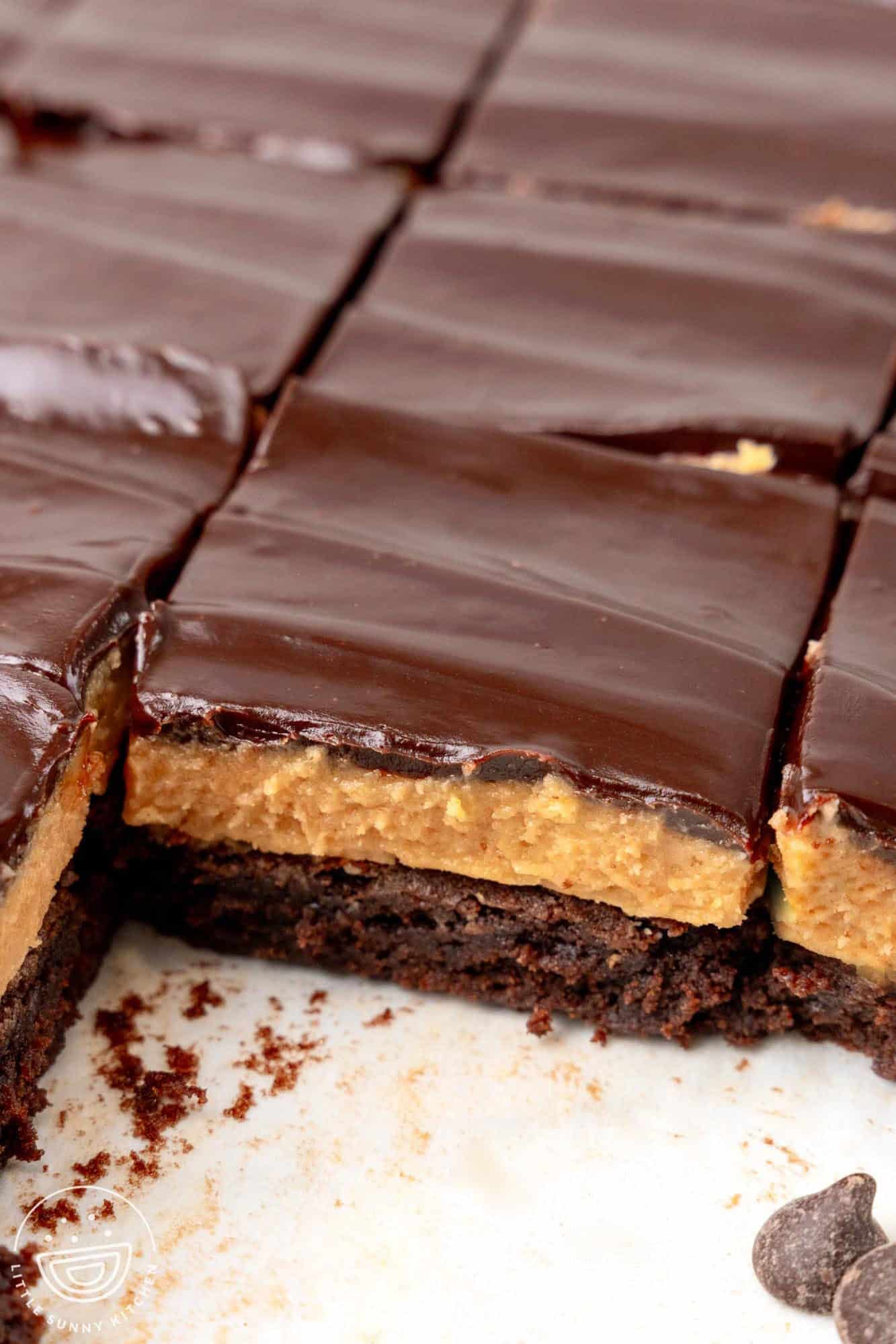 closeup of a cut pan of buckeye brownies. Two pieces have been removed to show the layers of brownie, peanut butter, and chocoalate.