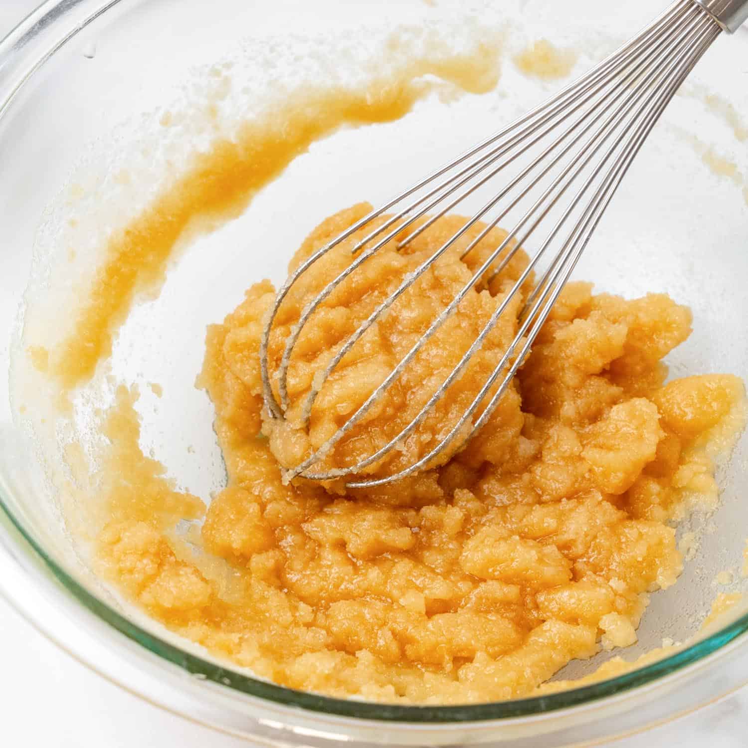 Oil and sugar whisked together in a glass bowl.