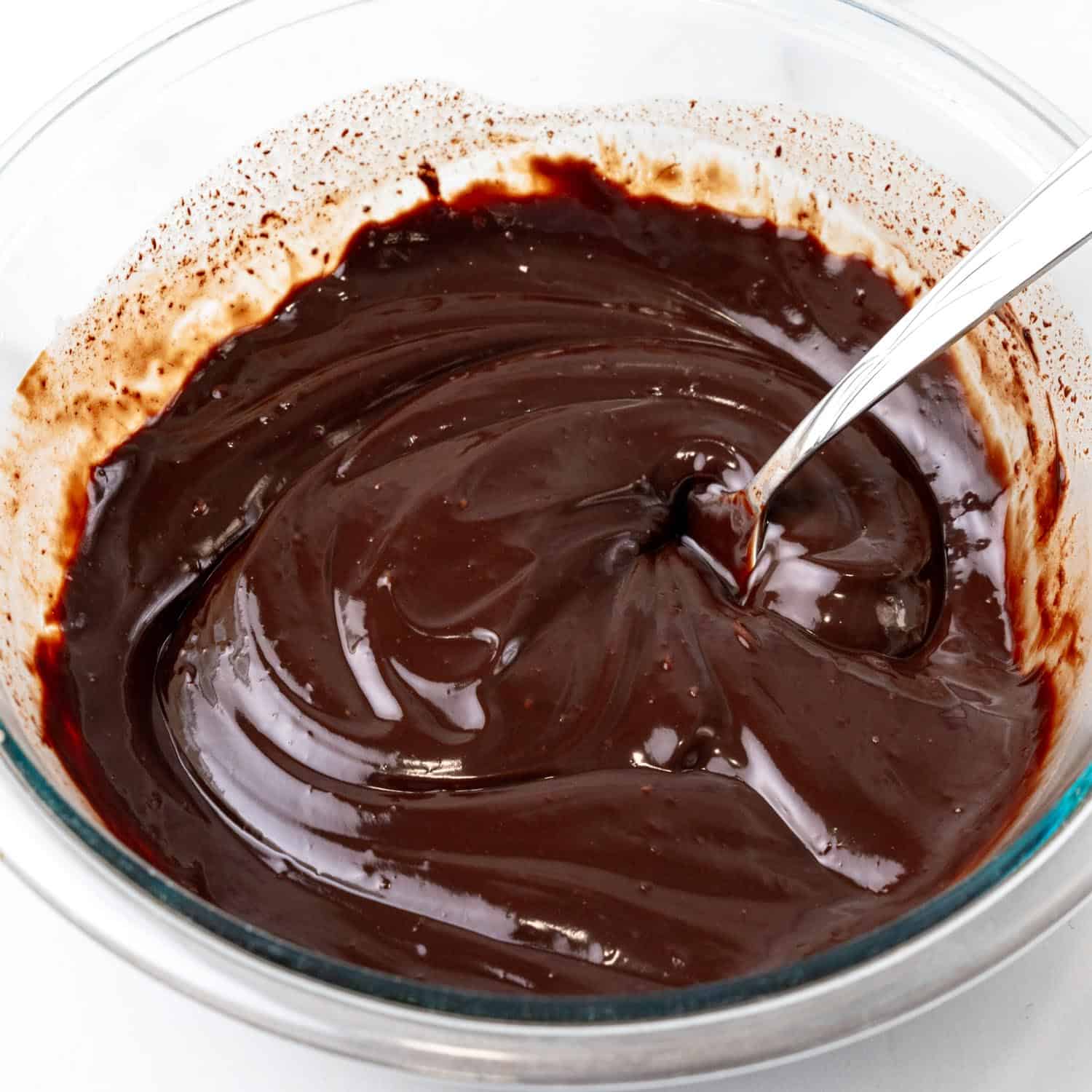 Melted chocolate in a small glass bowl with a metal spoon.