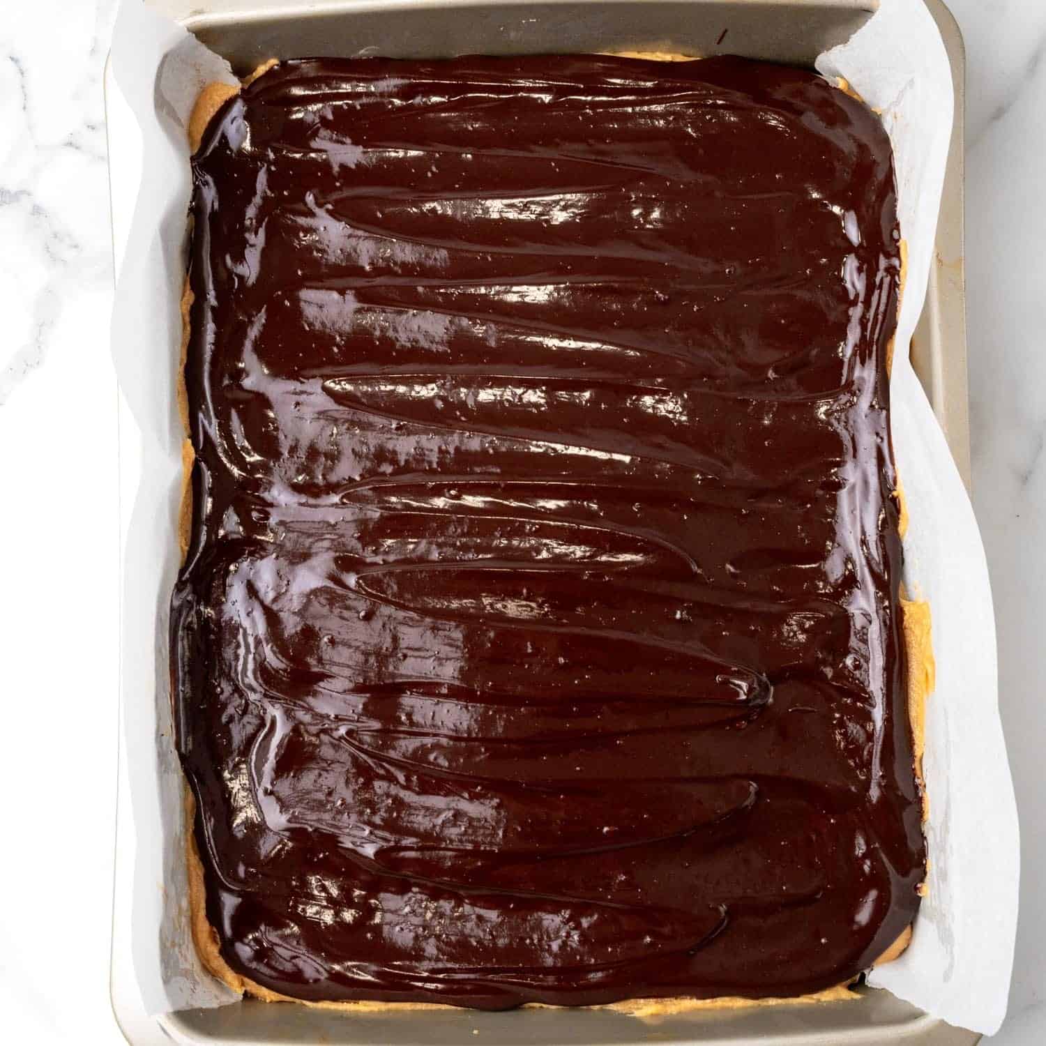 Melted chocolate spread over buckeye brownies in a metal baking pan.