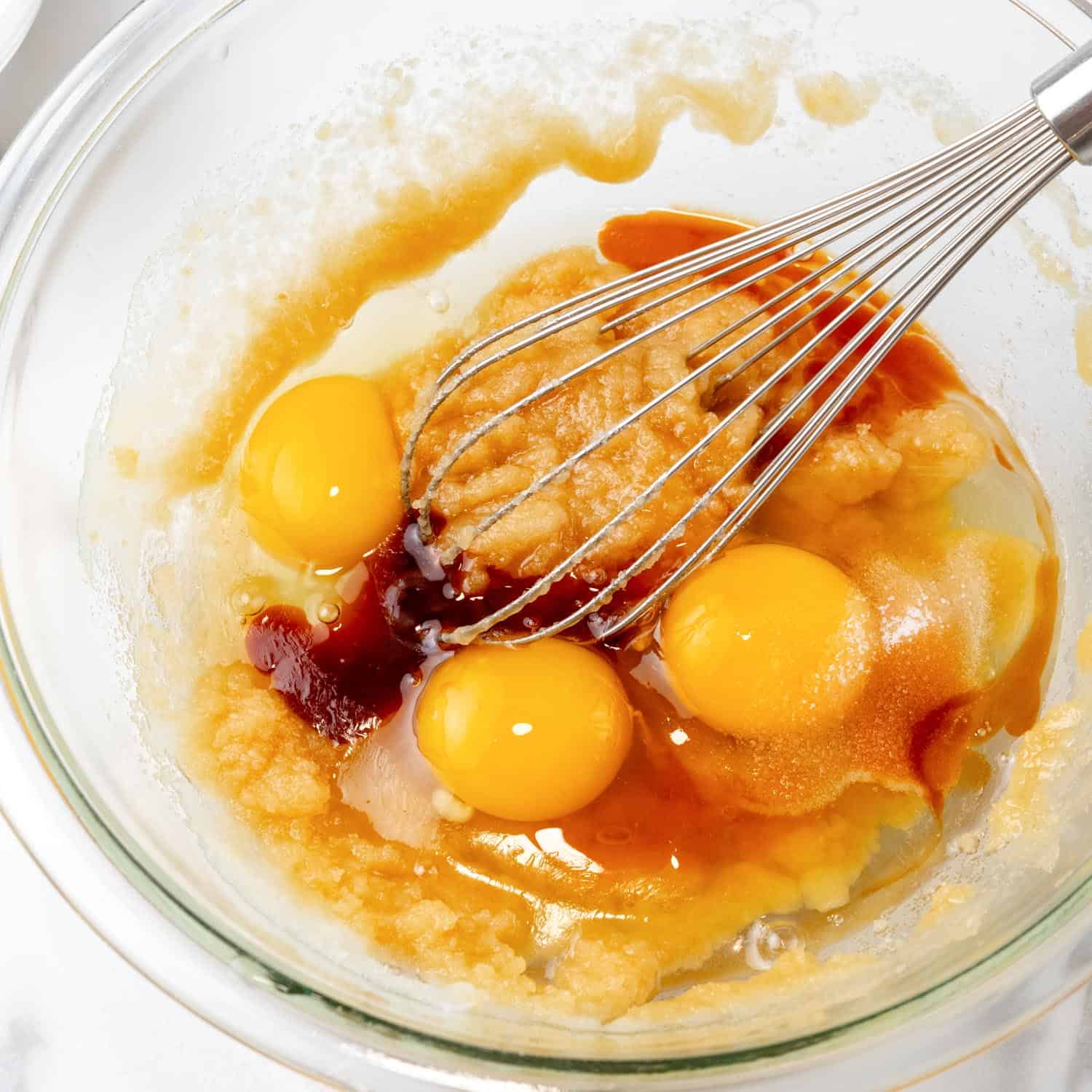 Eggs and vanilla added to batter in a small glass bowl with a wire whisk.