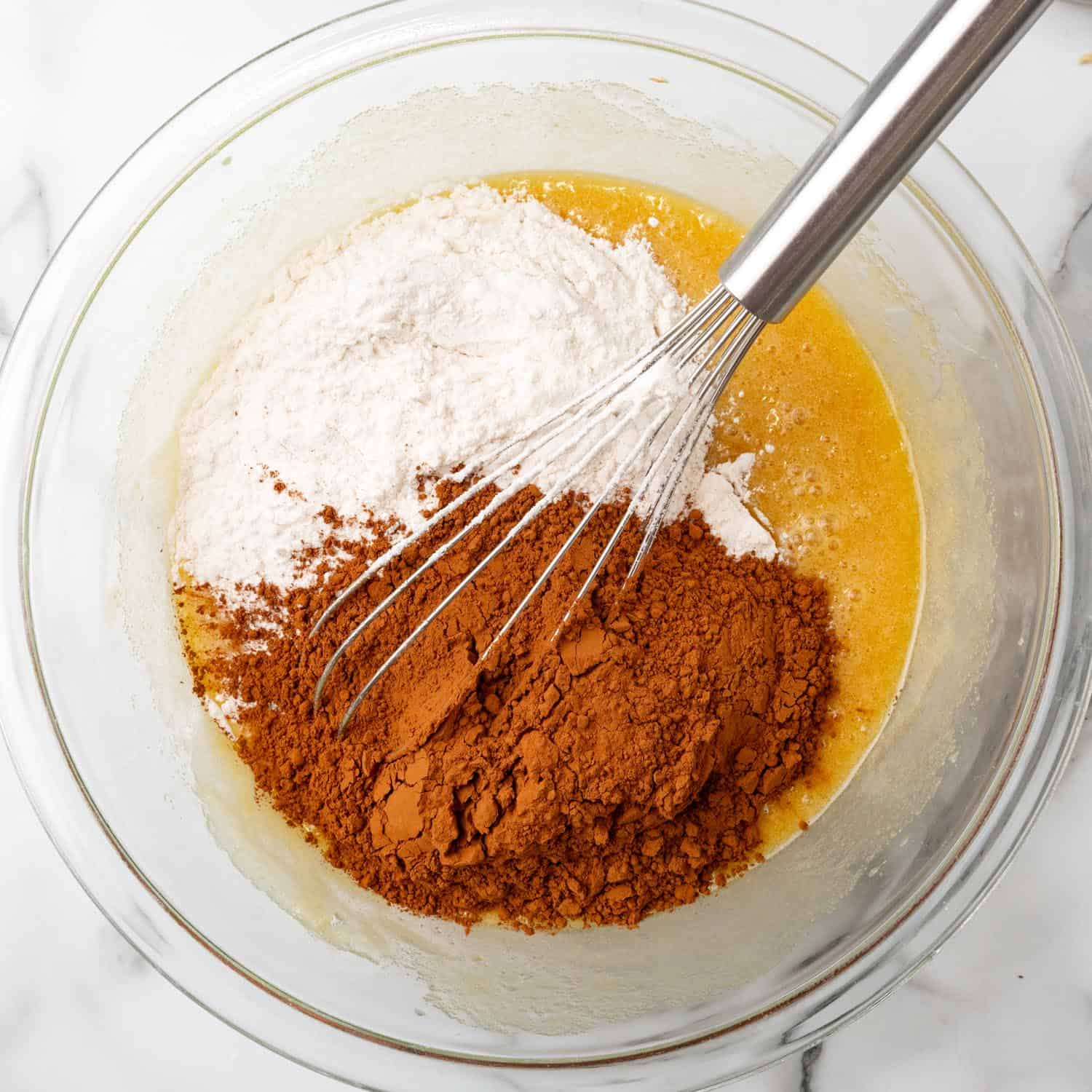 Flour and cocoa powder added to brownie batter in a bowl with a whisk.