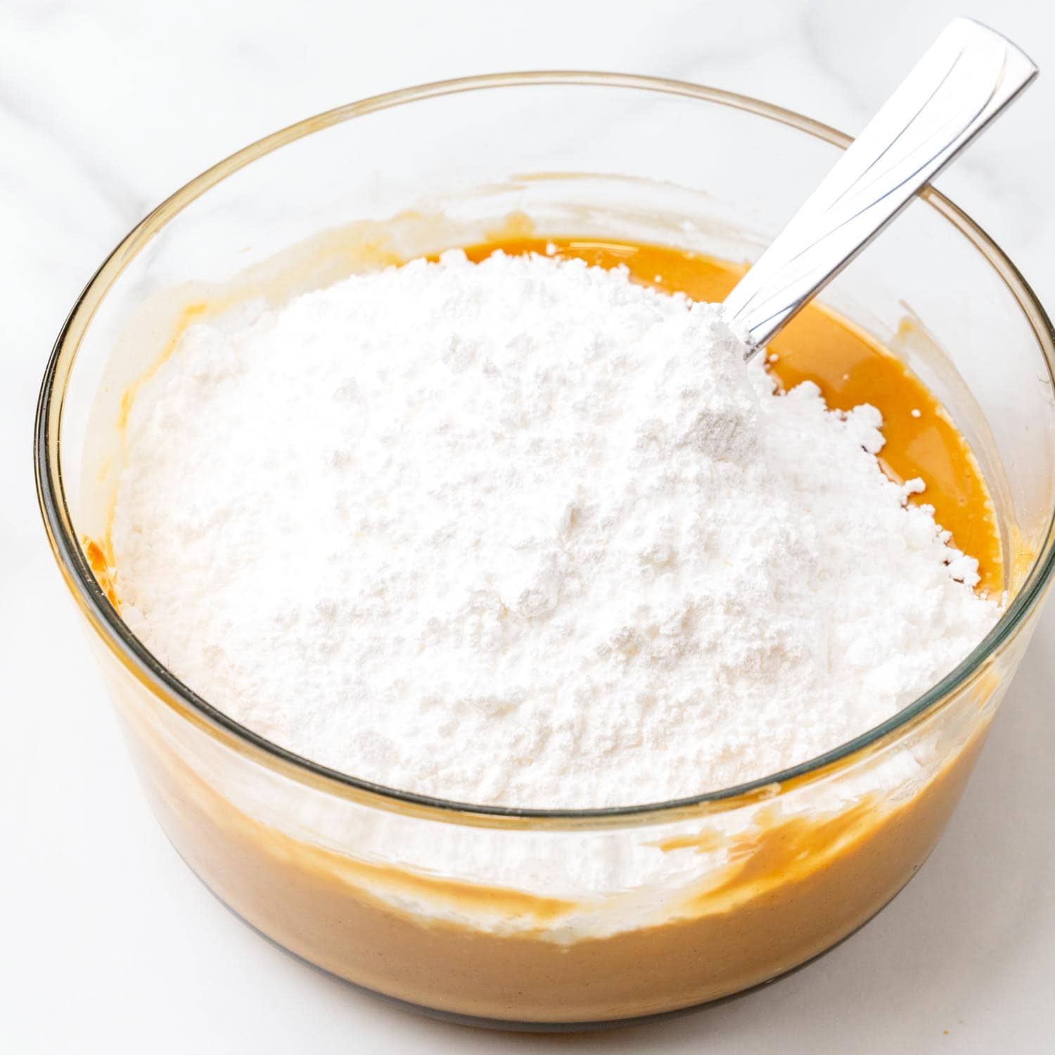 Powdered sugar added to melted peanut butter in a glass bowl.