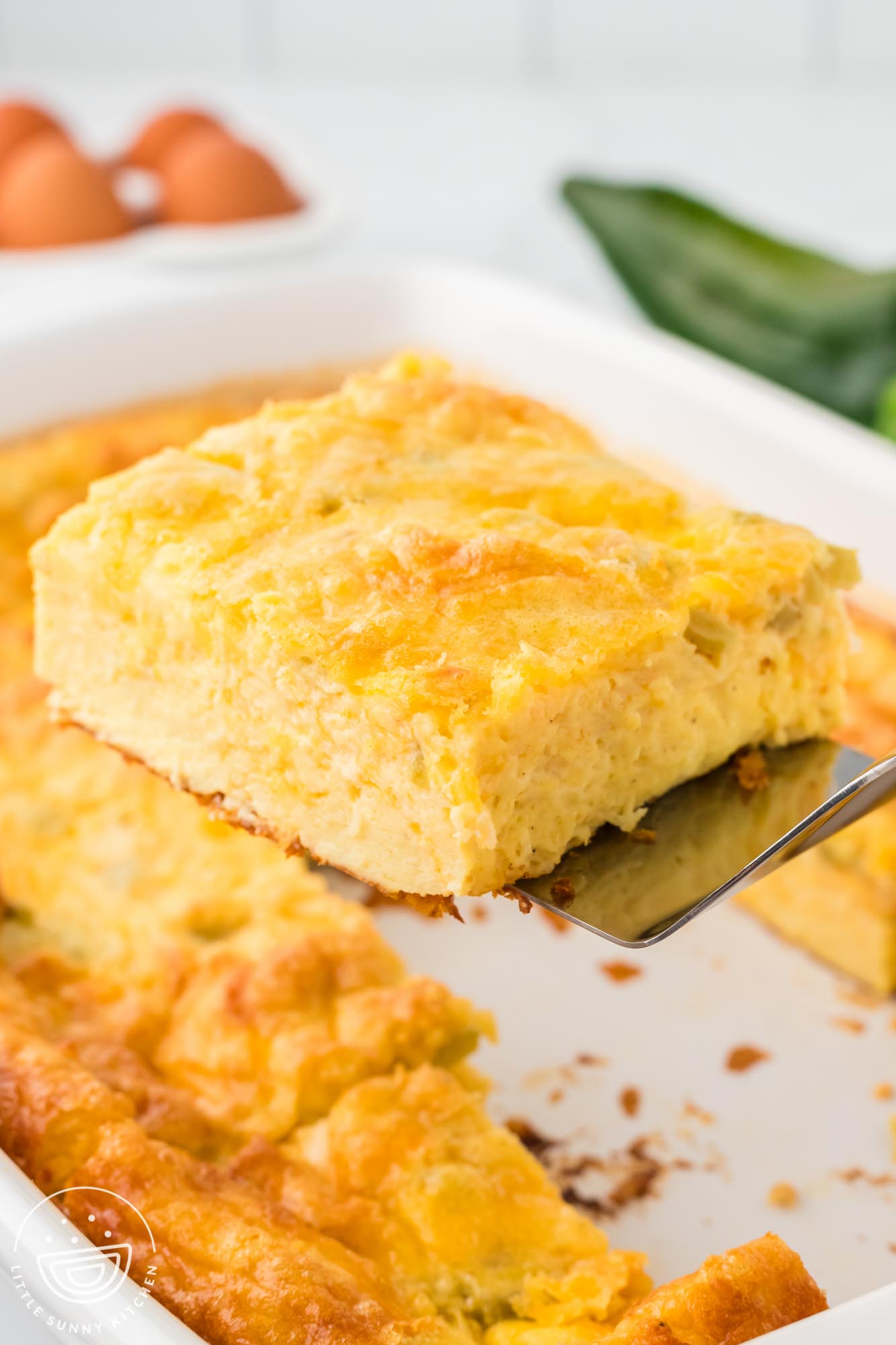 a spatula lifting a slice of egg casserole with cheese and green chilies out of a pan.