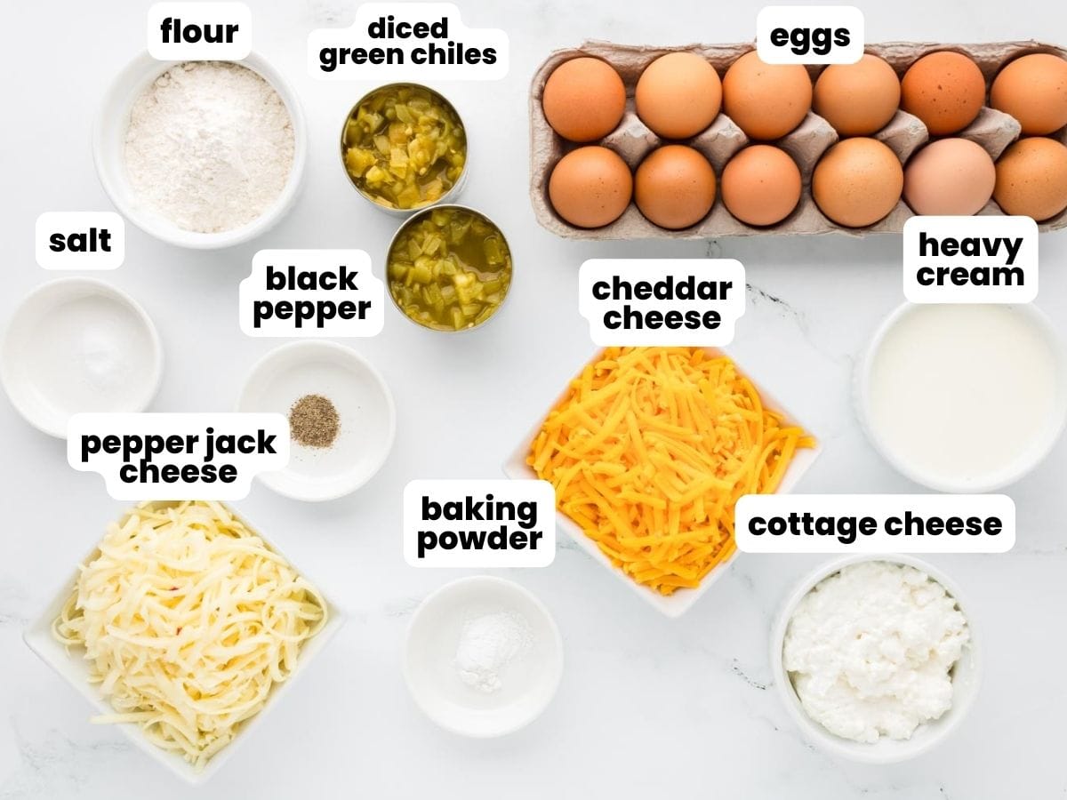 a dozen brown eggs next to two bowls of shredded cheese, cans of diced green chiles, cream, and seasonings, the ingredients for egg casserole.