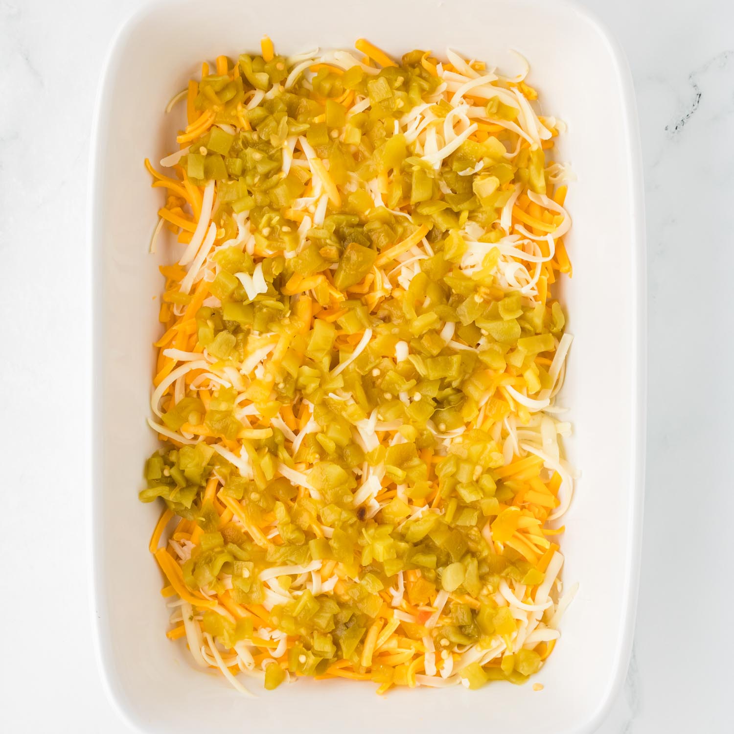 a white ceramic baking dish filled with shredded cheese and diced green chiles.