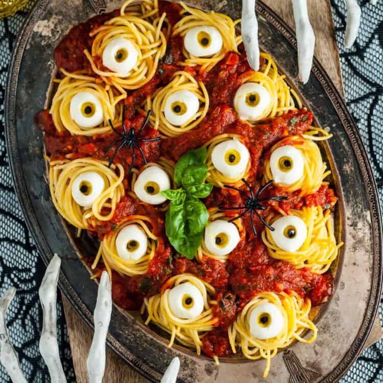 A platter of halloween spaghetti with mozzarella eyes on a spooky table with skeleton hand decorations.