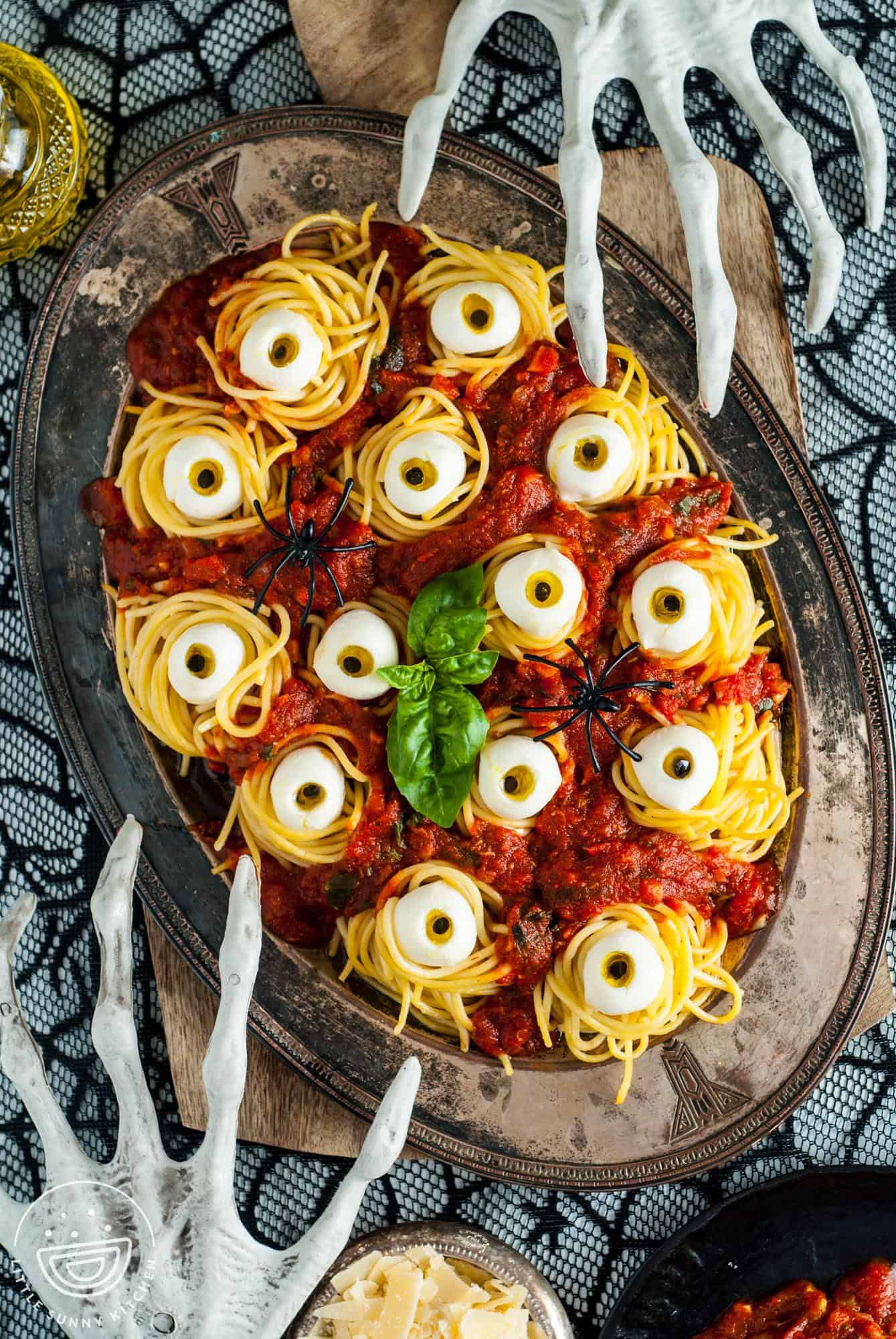 A platter of halloween spaghetti with mozzarella eyes on a spooky table with skeleton hand decorations.