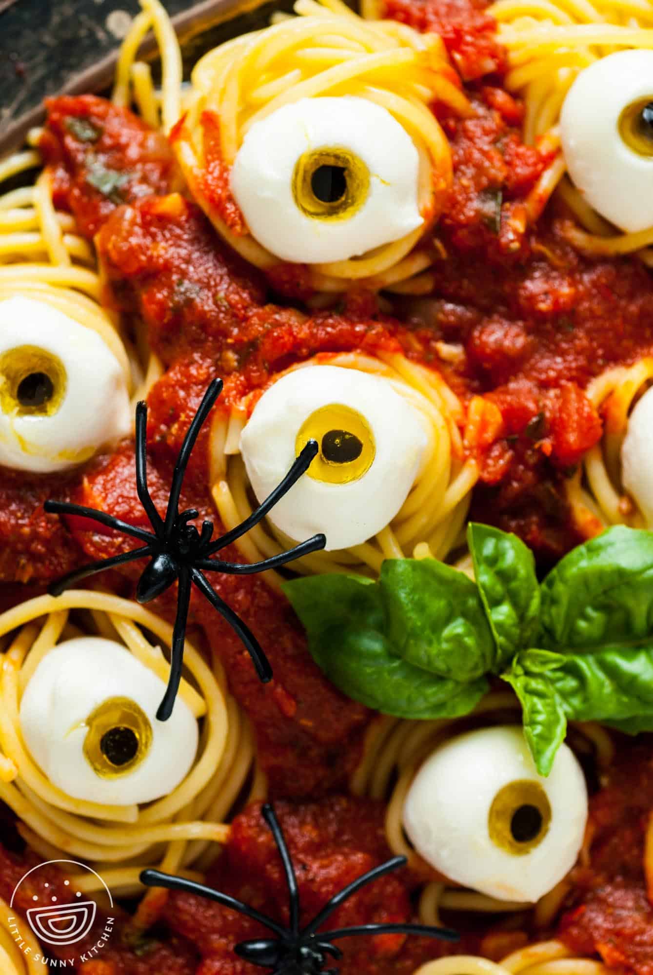 closeup of halloween spaghetti with cheese and olive eyeballs. A plastic spicer and fresh basil are added as garnish.